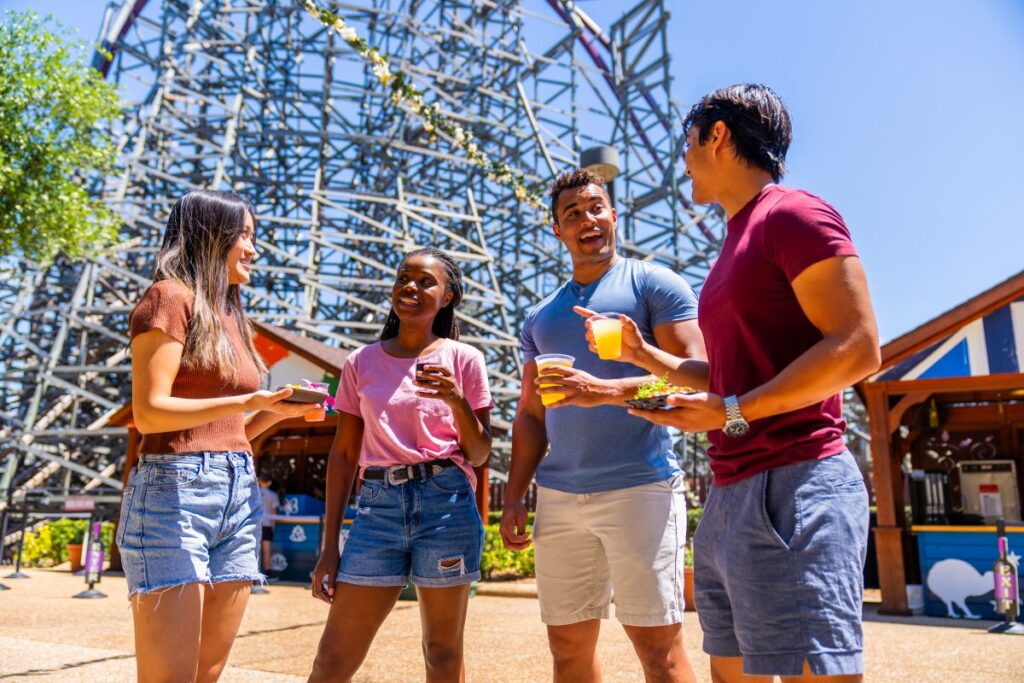Florida Platinum Pass reasons to buy- photo showing people enjoying a beverage in front of a roller coaster