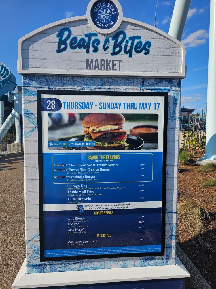 Signboard reading 'Beats & Bites Market' at Seven Seas Food Festival with a large menu board showing burger options and dates (Thu–Sun, thru May 17).