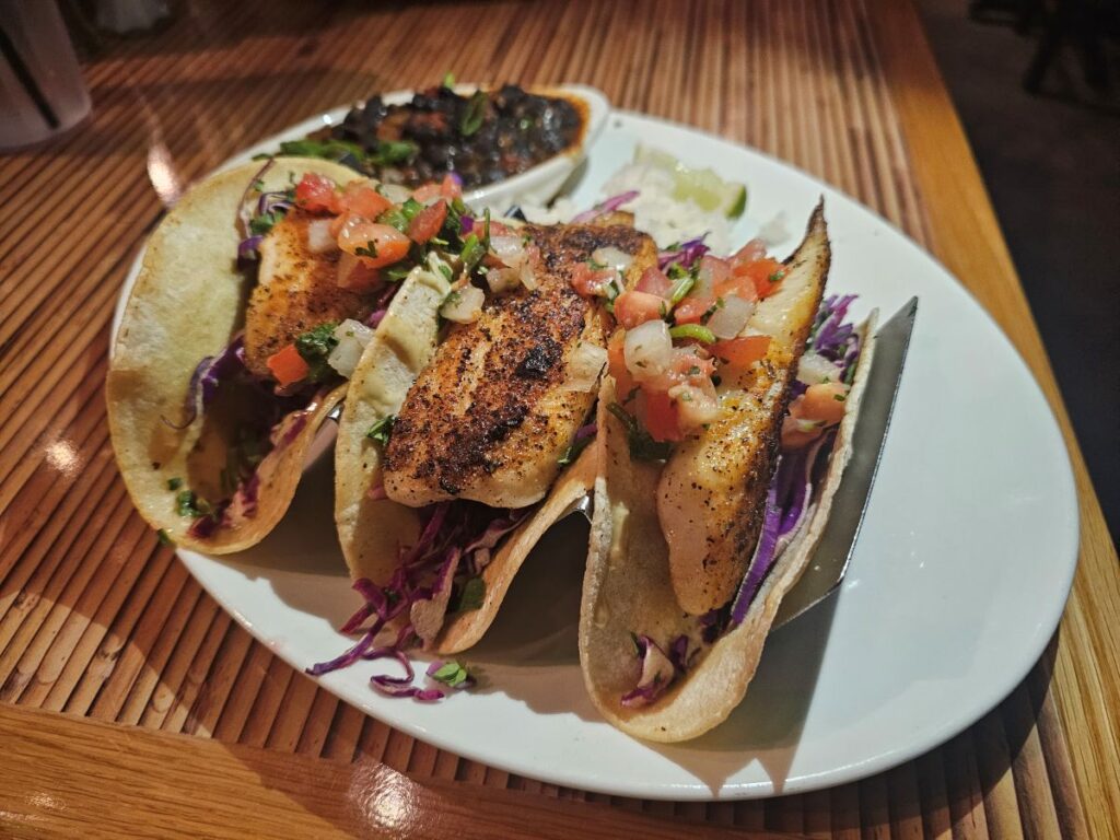Three Blackened Fish Tacos on a bright white plate with black beans seen in the background