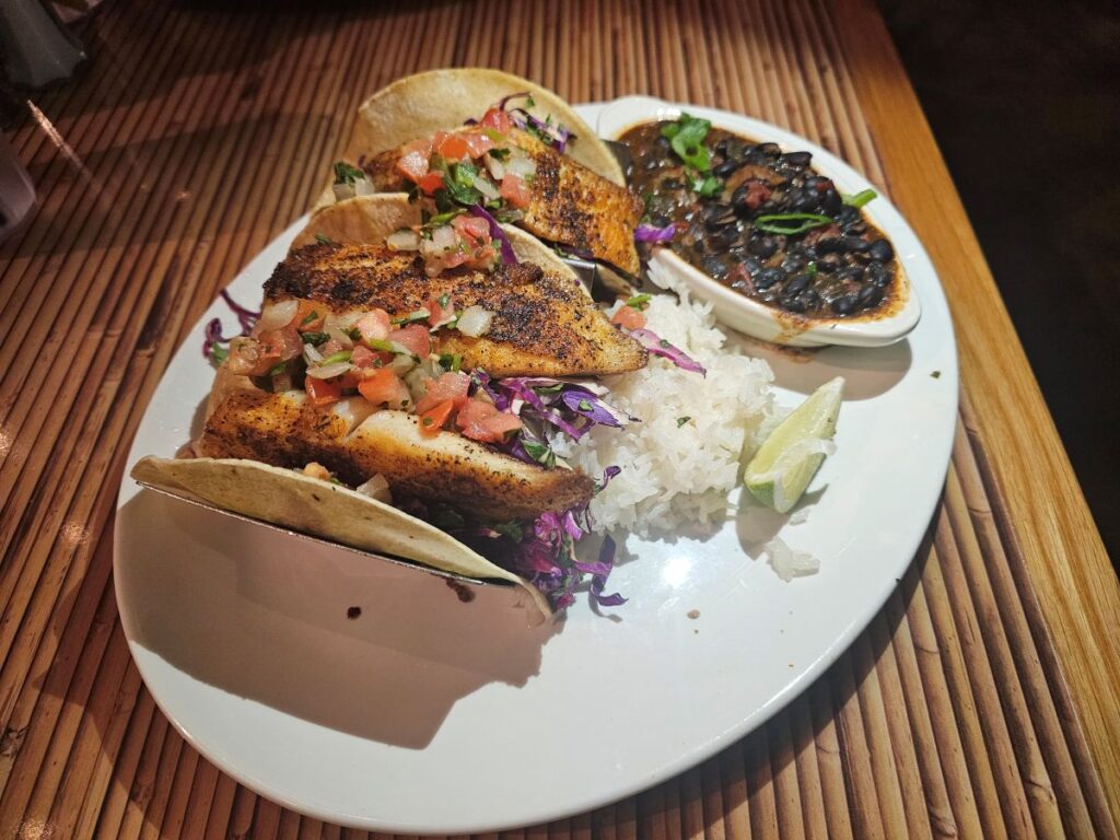 Three Blackened Fish Tacos with rice peaking out from underneath and black beans in a separate dish