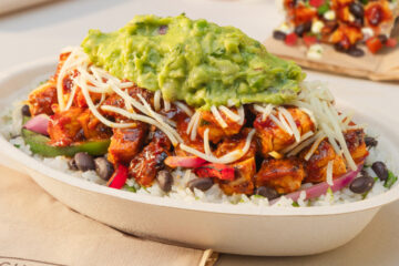 Burrito bowl with rice, black beans, fajita veggies, spicy chicken, shredded cheese, and a scoop of guacamole on top