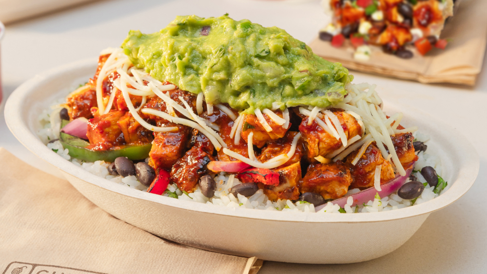 Burrito bowl with rice, black beans, fajita veggies, spicy chicken, shredded cheese, and a scoop of guacamole on top