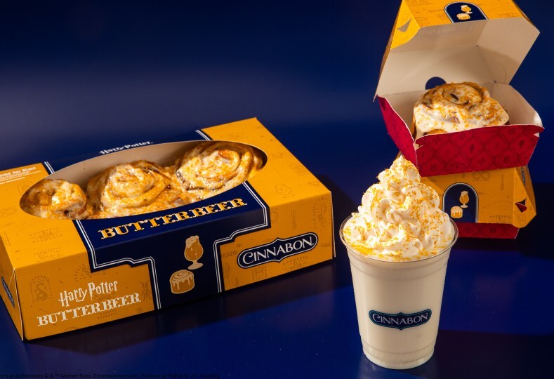 Butterbeer boxes with pastries and a whipped-cream drink on a blue surface, part of a Harry Potter display