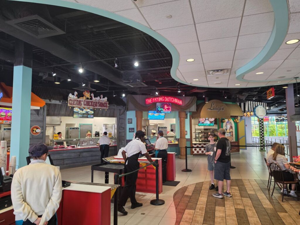 Food court scene with counter-service stalls, including signs for The Frying Dutchman and Luigi's, as customers order and dine nearby.