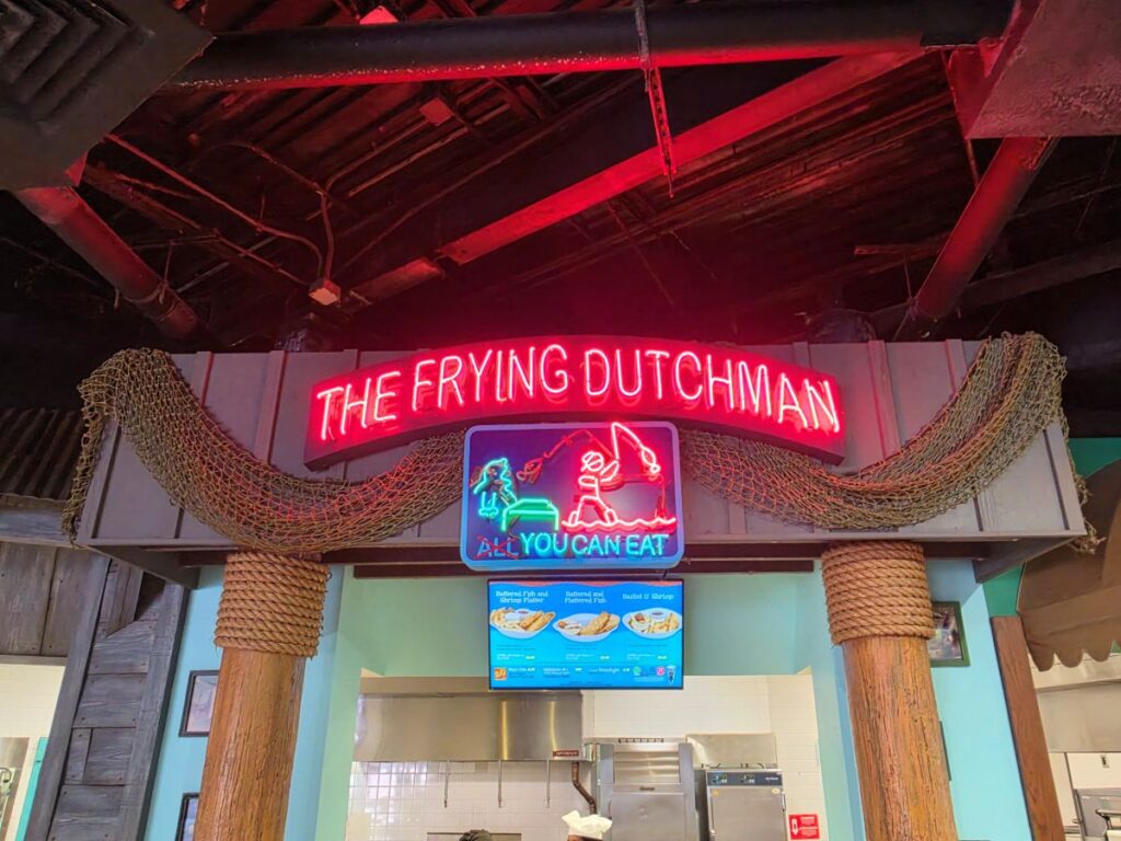 Neon sign reading 'THE FRYING DUTCHMAN' above a blue 'All You Can Eat' sign in a tropical-themed restaurant.
