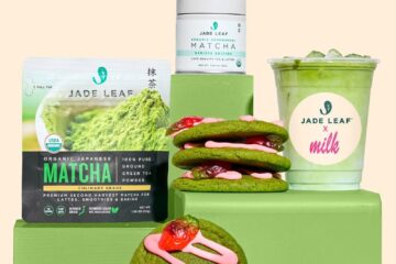 Jade Leaf matcha display with powder pouch, tin, green cookies with pink icing, and a milk matcha drink on a green pedestal.