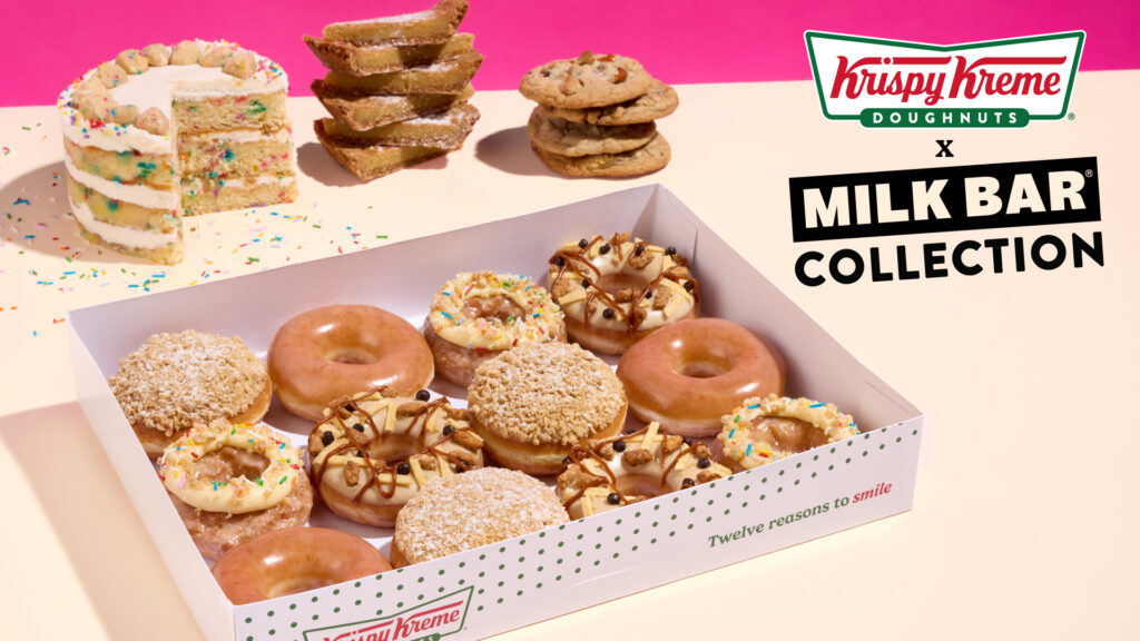 Box of assorted Krispy Kreme Milk Bar donuts in a white tray, with cakes and cookies in a pink studio backdrop.