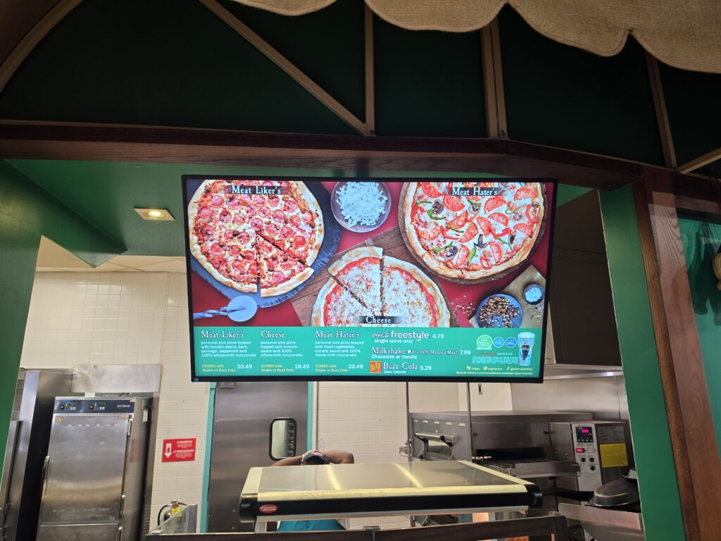 Digital Fast Food Boulevard menu board showing two pizzas labeled 'Meat Liker's' and 'Meat Hater's' in a green restaurant interior.
