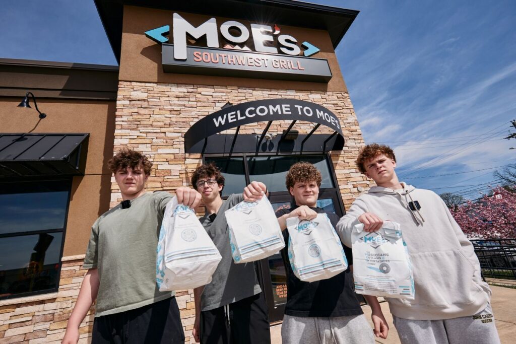 Four young men stand outside Moe's Southwest Grill, each holding white takeout bags.