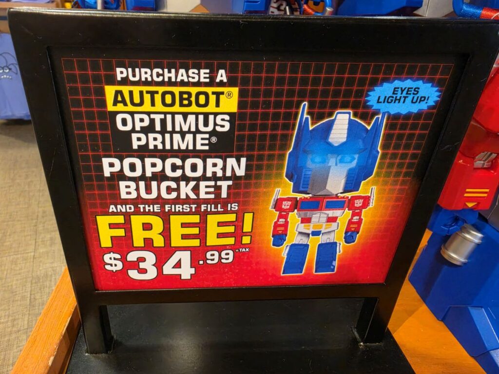 Sign promoting an Autobot Optimus Prime popcorn bucket: first fill is free, price $34.99, with a blue robot image.
