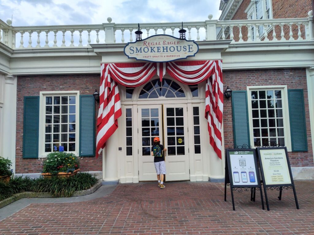 Restaurant entrance with white double doors, red-and-white striped fabric, and a sign reading 'Smokehouse' above; a child stands at the door.