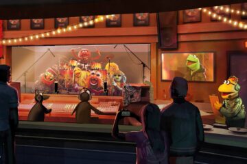 Colorful Muppet band performing on a recording-studio stage behind glass, audience silhouettes watching under string lights.