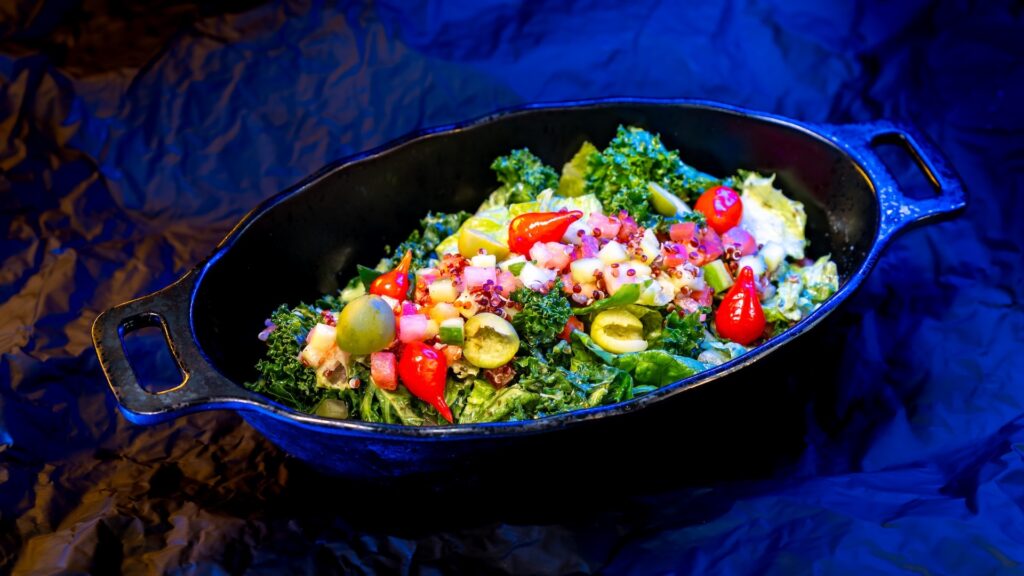 Colorful kale salad with olives, peppers, and diced veggies in a black skillet.