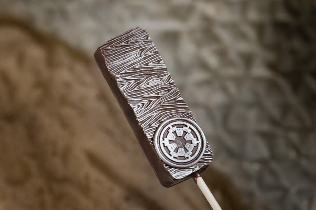 Close-up of a dark chocolate bar with a swirled, wood-grain pattern on a metallic clip, against a blurred background, an example of Mandalorian Grogu Disney food