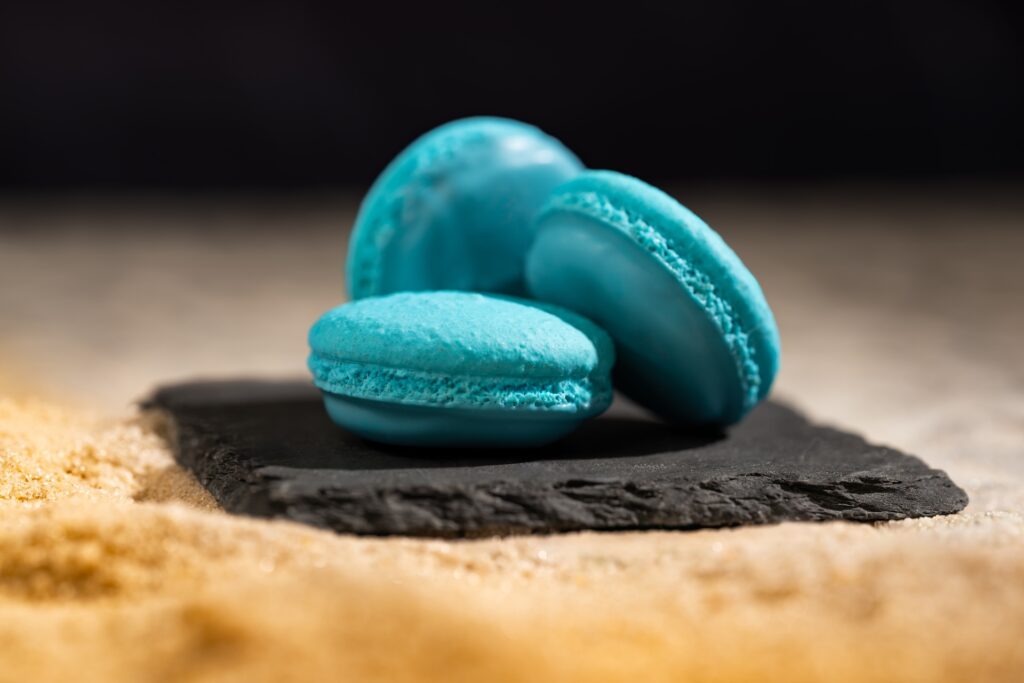 Three turquoise macarons stacked on a dark slate with a sandy foreground, an exmaple of Mandalorian Grogu Disney food