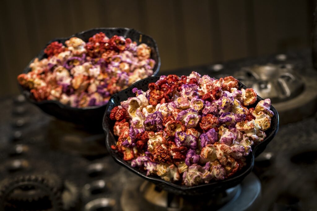 Two black bowls filled with colorful caramel popcorn on a dark blurred background.