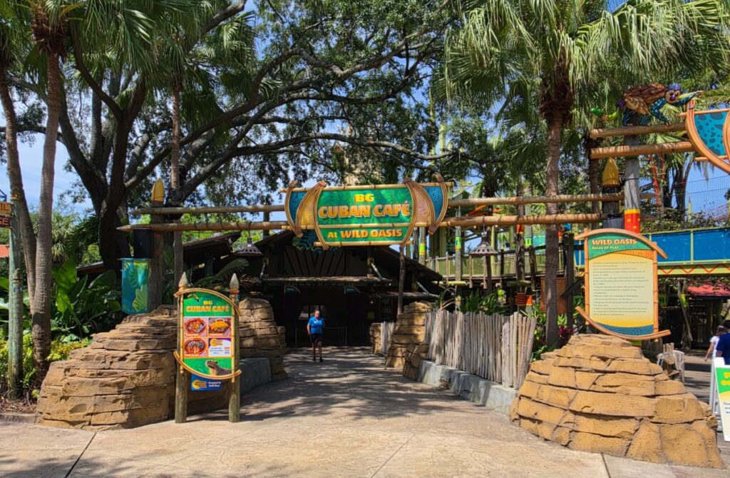Entrance to BG Cuban Café at Wild Oasis, tropical entrance with palm trees and stone pillars and a colorful sign above the doorway