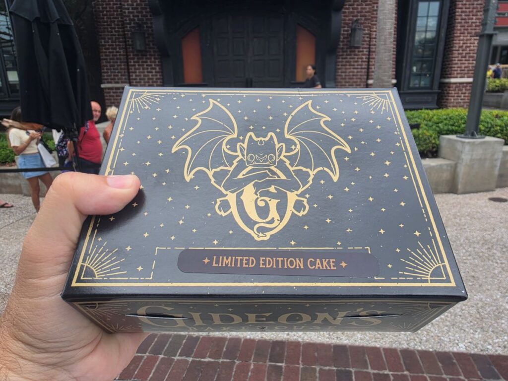 Black cake box holding the Blueberry Lemonade Cake with a gold dragon logo and stars, labeled 'Limited Edition Cake', held outdoors by a hand