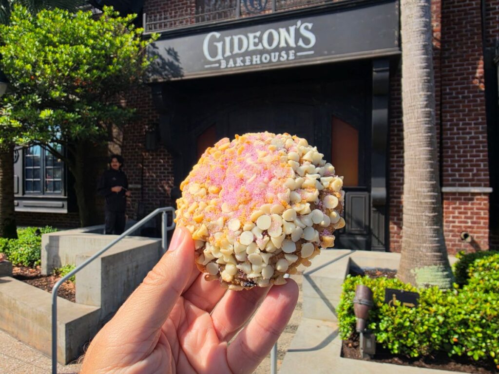 Close-up of a Blueberry lemonade Cookie held in a hand in front of Gideon’s Bakehouse storefront.