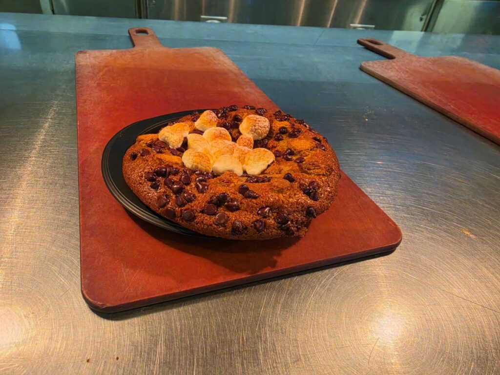 Café 4 S'mores Cookie with toasted marshmallows on a red cutting board in a kitchen setting.