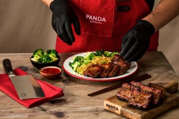 Panda Express chef in a red apron plates sliced glazed pork ribs with broccoli and noodles on a white dish for new Cantonese BBQ Brisket