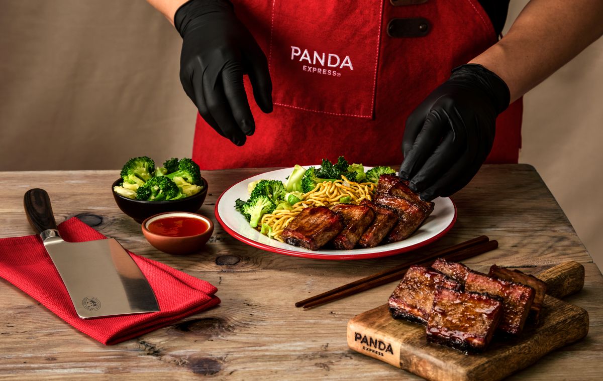 Panda Express chef in a red apron plates sliced glazed pork ribs with broccoli and noodles on a white dish for new Cantonese BBQ Brisket