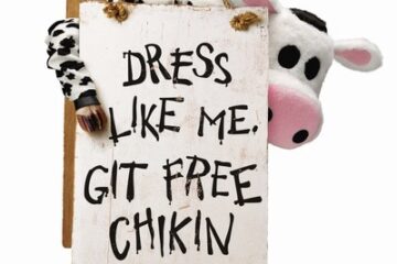 Person in a cow costume holds a sign reading 'DRESS LIKE ME, GET FREE CHIKIN' with a plush cow peeking from behind the sign fro Cow Appreciation Day returns