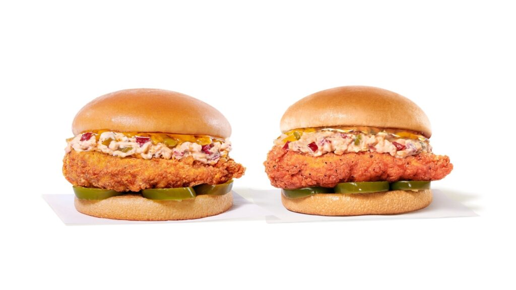 Two fried chicken sandwiches with pickles, creamy sauce, and buns on a white background.