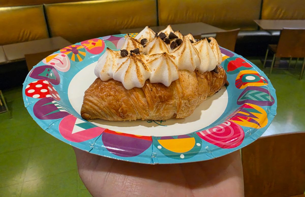 Chocolate Marshmallow Hazelnut Croissant with whipped cream peaks and chocolate chips on a bright, decorative plate in a cafe setting.