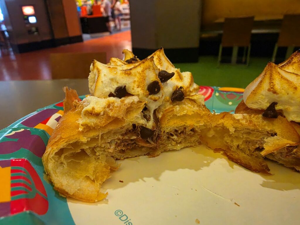 Flaky pastry with cream topping and chocolate chips on a colorful plate at a cafe, with a bite taken out of it.