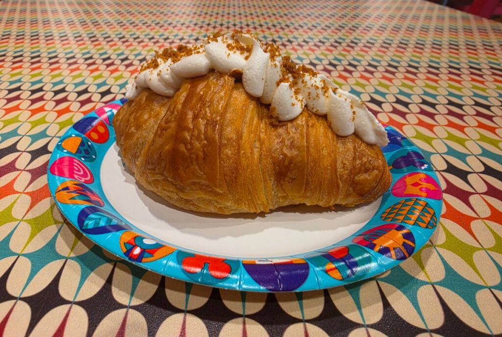 Cookie Butter Croissant topped with piped whipped cream and crumbs on a bright, colorful plate.