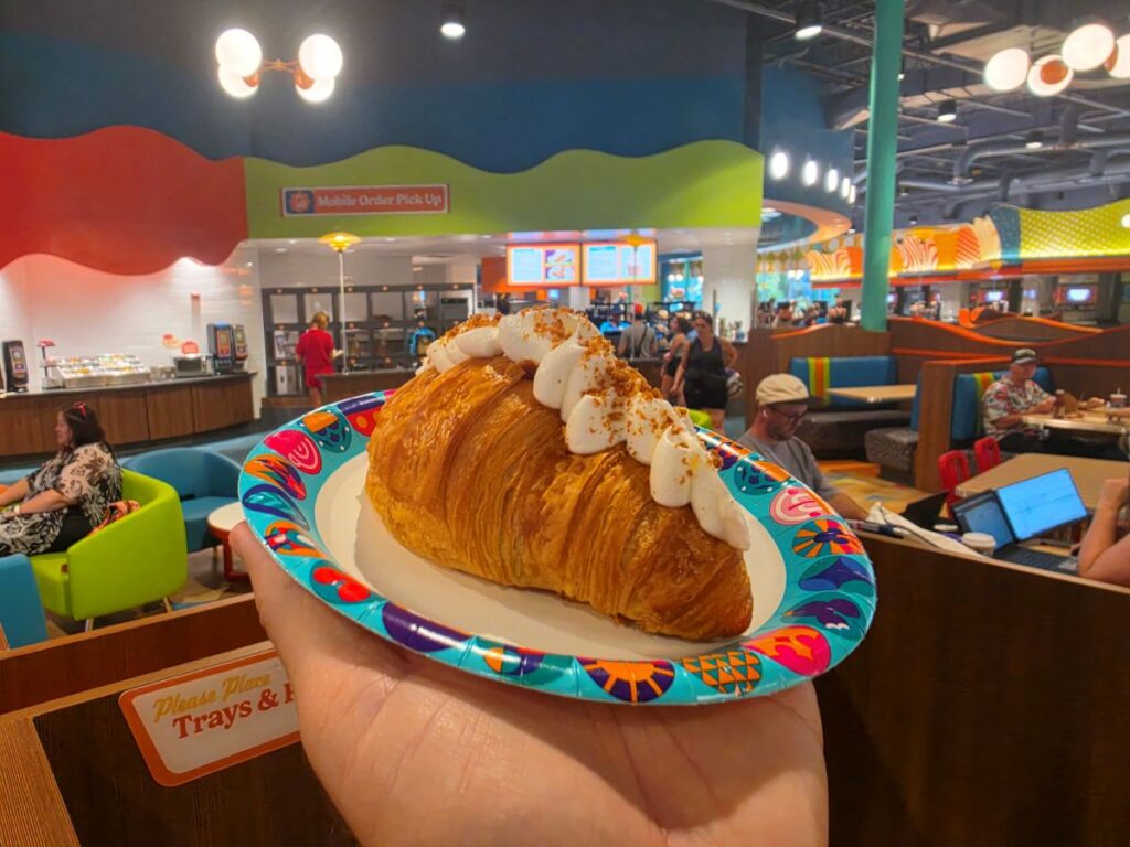 Cookie Butter Croissant with cream dollops on a bright patterned plate, held in a lively, colorful restaurant.