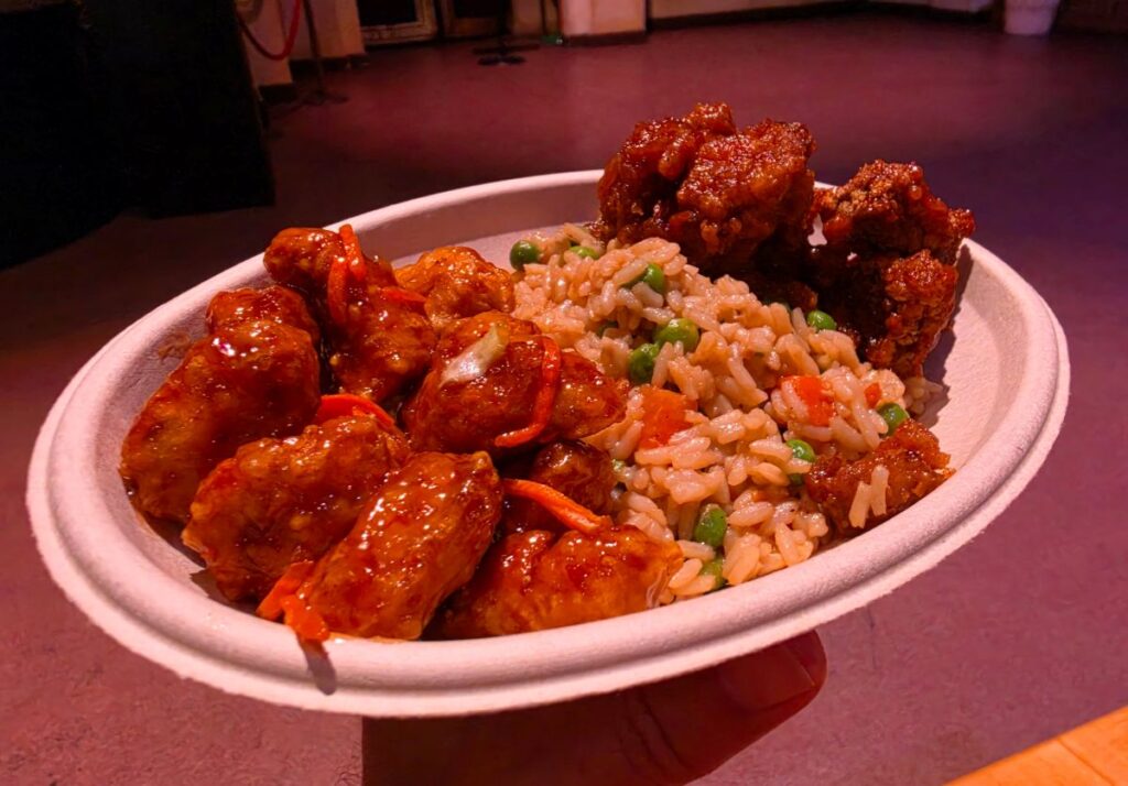 Plate of saucy fried chicken bites and fried rice with peas and carrots.