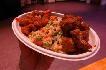 Paper plate with glazed fried chicken bites and vegetable fried rice (peas and carrots) held in a hand indoors for a Dragon Fire Grill review
