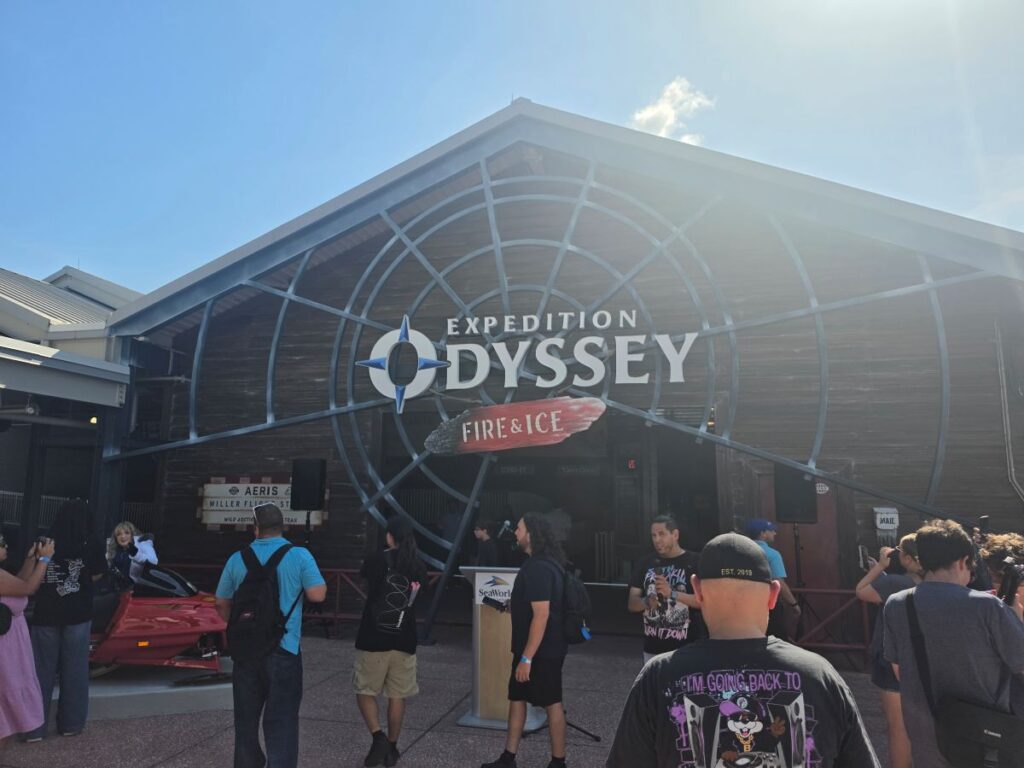 Exterior view of Expedition Odyssey: Fire & Ice attraction with a large circular blue logo on the façade and visitors gathered outside.
