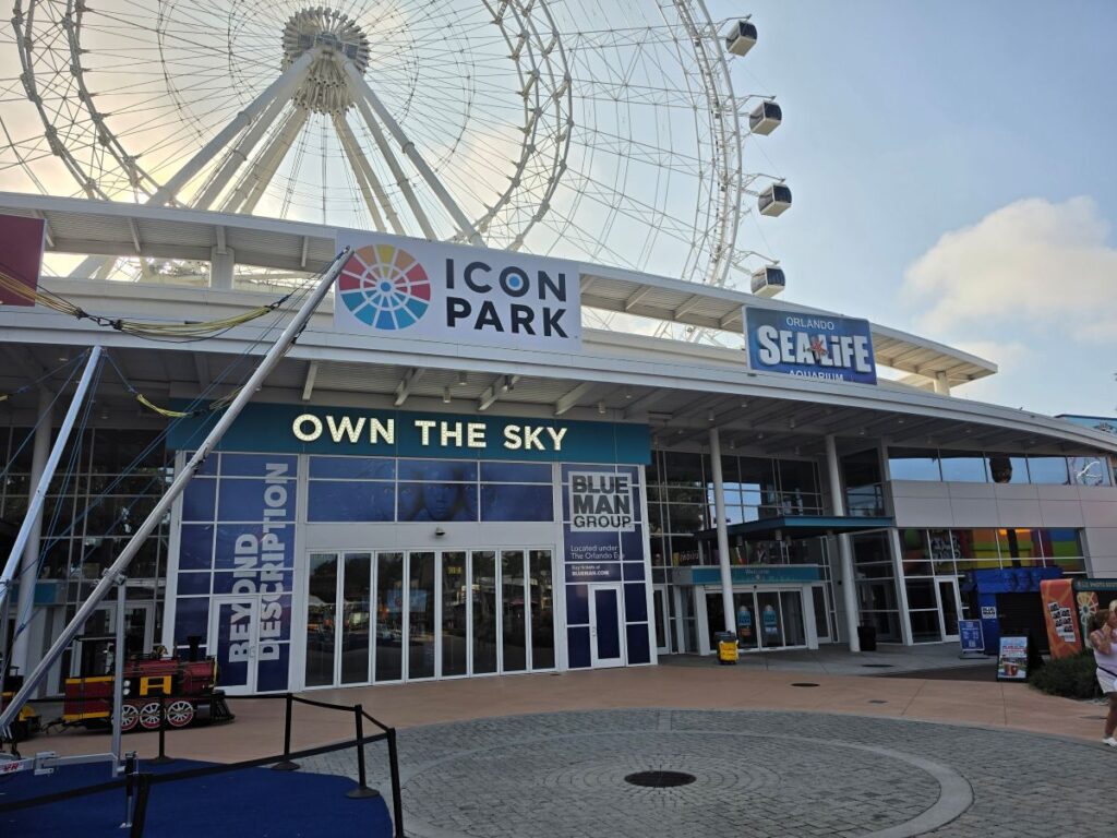 Entrance to Sea Life Orlando with a large Ferris wheel overhead and signs reading 'Icon Park' and 'Own The Sky'.