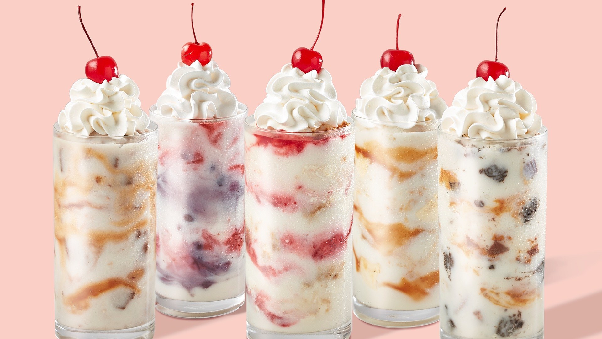 Row of six tall milkshakes topped with whipped cream and a cherry on a peach background, lined up for a dessert banner promoting Freddy's Custard Tour