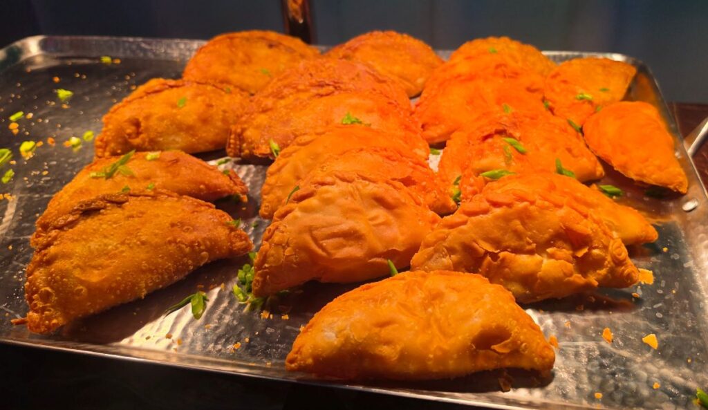 Stack of golden fried empanadas on a stainless steel tray, garnished with chopped cilantro.