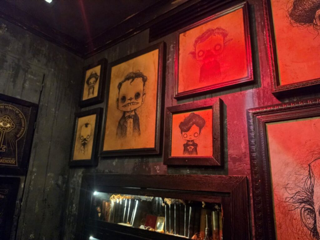 Wall adorned with framed eerie cartoon sketches in warm red light.