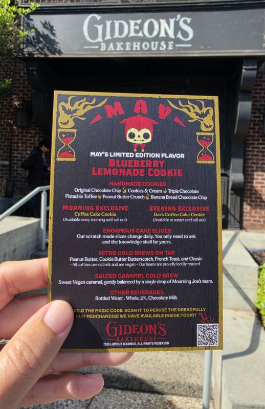 Hand holding a Gideon's Bakehouse flyer outside the shop, advertising May's limited edition Blueberry Lemonade Cookie flavors.