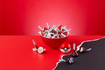 Red bowl overflowing with Pokémon-themed candies wrapped in red foil on a red surface.