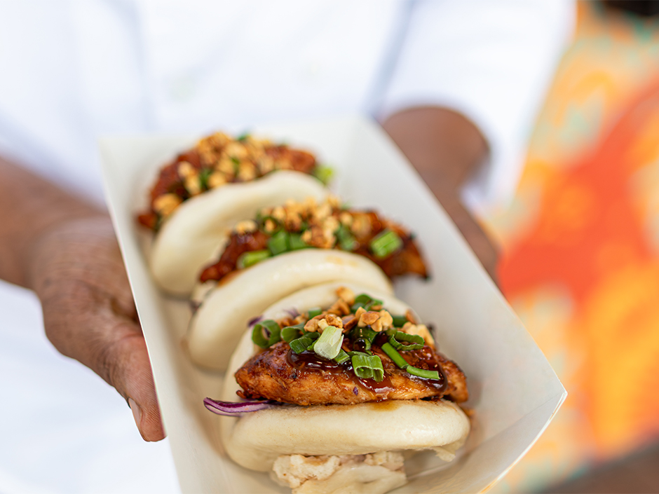 Three bao buns for theUniversal AANHPI Menu with glazed fried chicken, chopped green onions, and crushed nuts on a white tray.