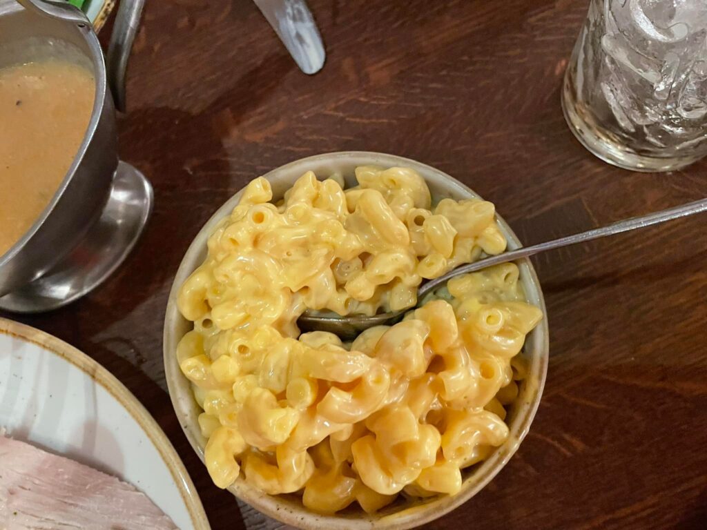 Creamy macaroni and cheese in a small bowl on a dark wooden table with a metal pitcher nearby from our Liberty Tree Tavern review