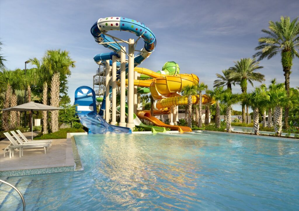Colorful multi-slide water park structure above a large pool, with palm trees surrounding the area.