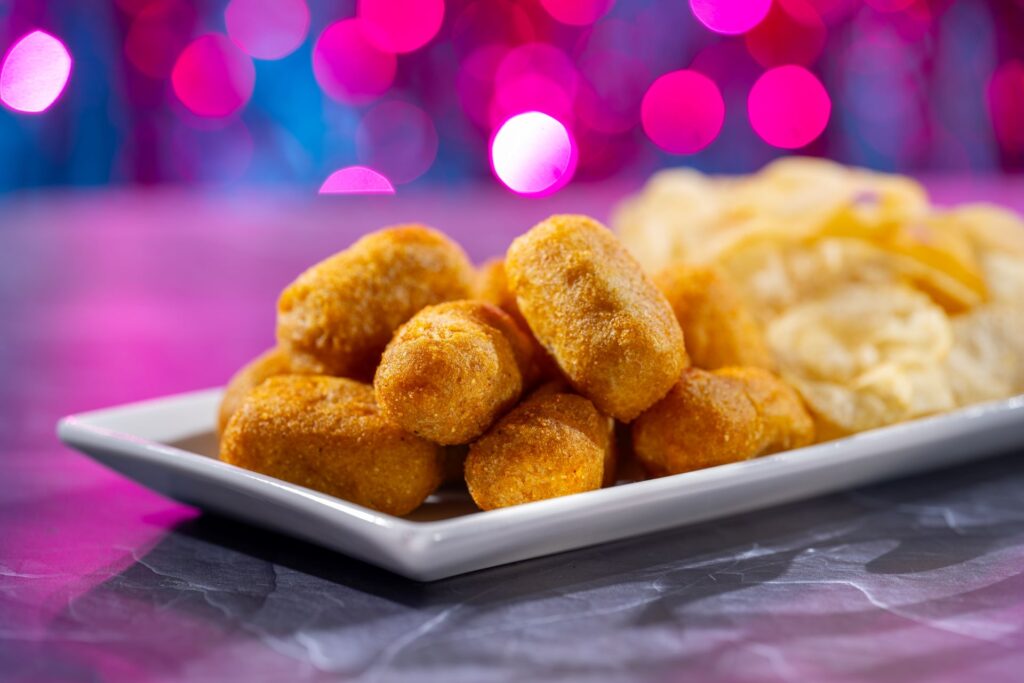 Plate of golden fried corn dog nuggets piled on a white dish against a vibrant pink and purple bokeh background for FØØD by Swedish Chef
