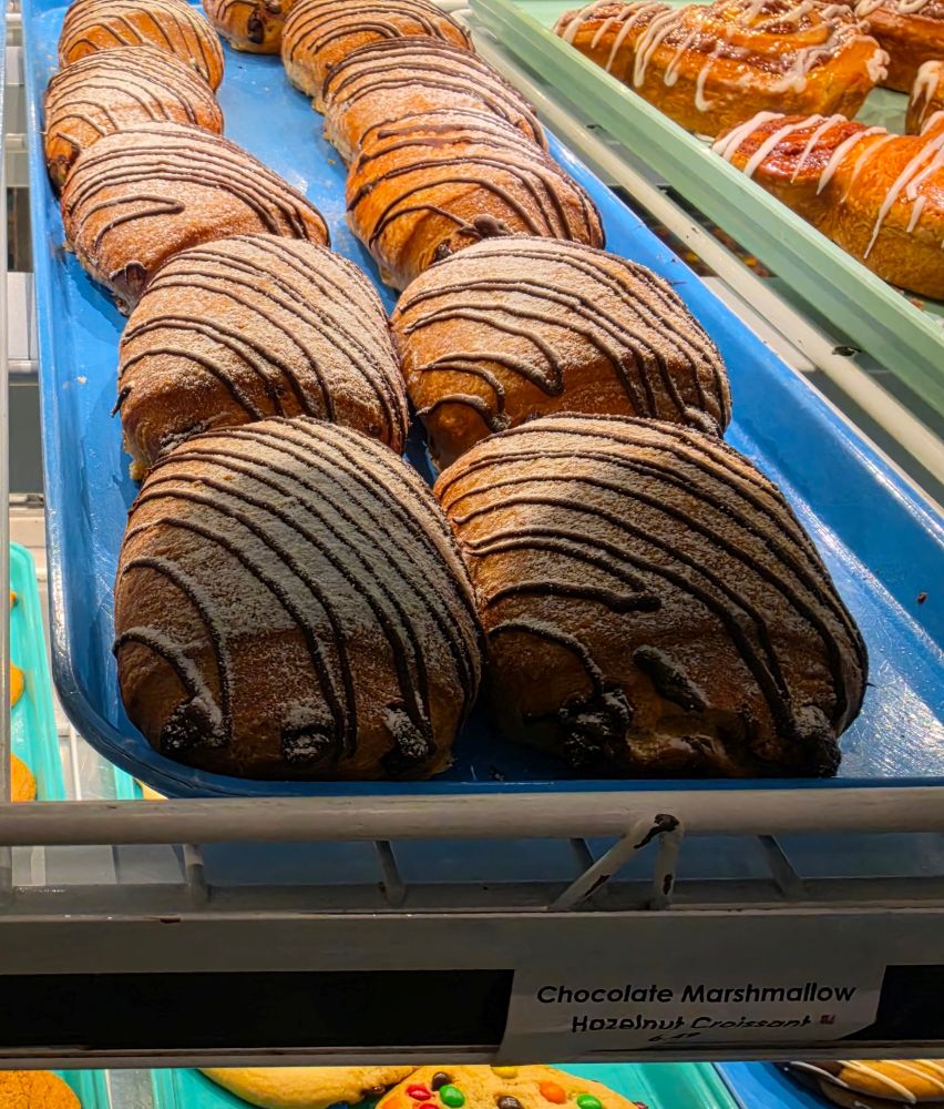 Row of chocolate marshmallow pastries on a blue bakery tray, lightly dusted with sugar and drizzled with chocolate.
