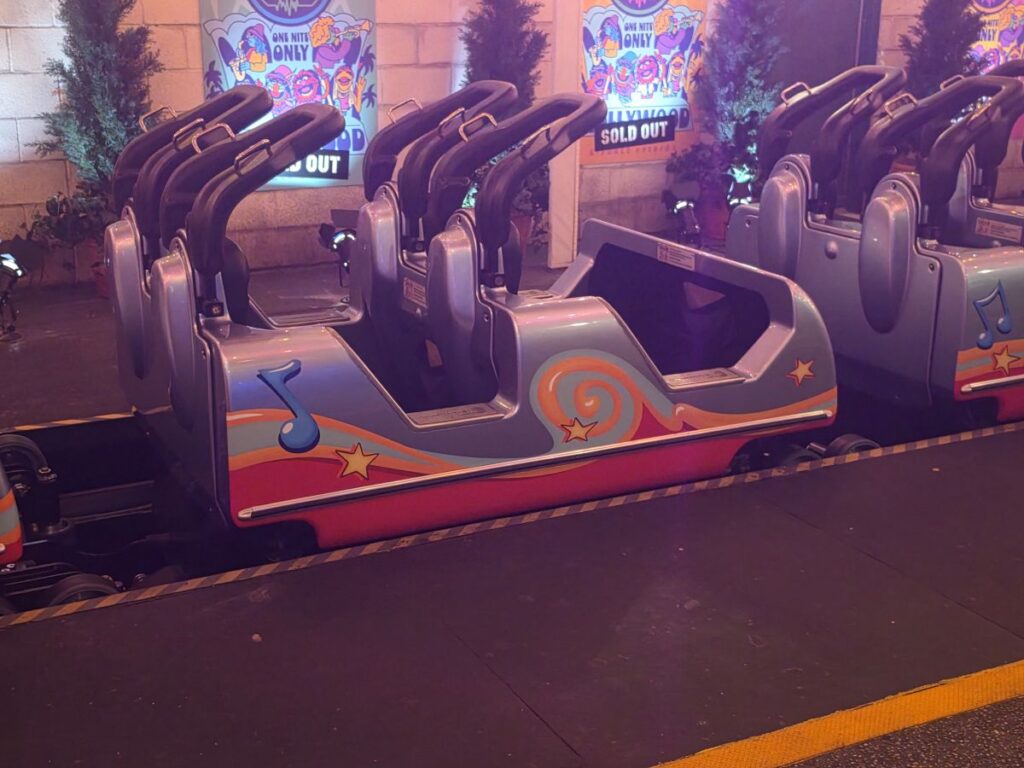 Colorful Muppets Rock 'n' Roller Coaster cars lined up on a track indoors; posters reading 'Sold Out' visible in the background.