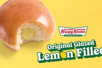 Close-up of a glazed lemon-filled doughnut with a bite taken out, featuring a yellow background and Krispy Kreme branding.