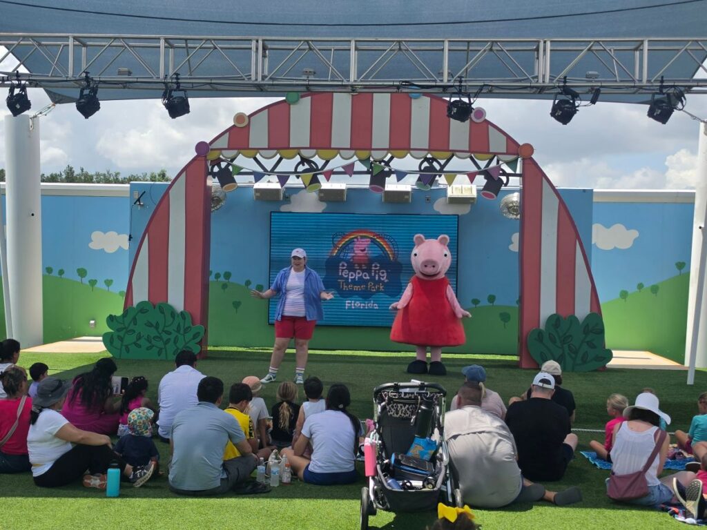 Peppa Pig Theme Park audience watches a stage show at Peppa Pig Theme Park Florida; a performer and a pink pig character entertain kids on stage.