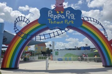 Entrance to Peppa Pig Theme Park with a large rainbow arch and a blue sign featuring Peppa Pig logo.
